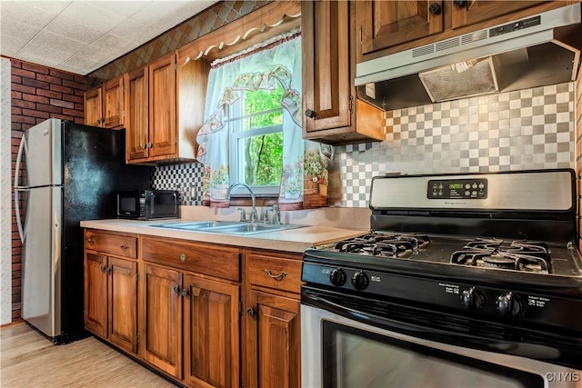 kitchen with under cabinet range hood, stainless steel appliances, a sink, and light countertops