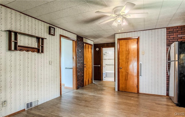 spare room with wallpapered walls, visible vents, baseboards, ceiling fan, and wood finished floors