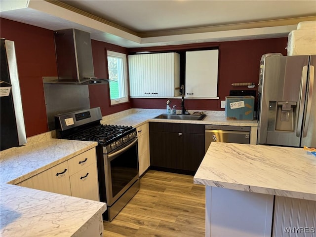 kitchen featuring stainless steel appliances, a sink, light countertops, wall chimney exhaust hood, and light wood finished floors