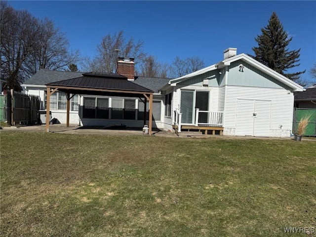 rear view of property with a lawn, a chimney, metal roof, fence, and a gazebo