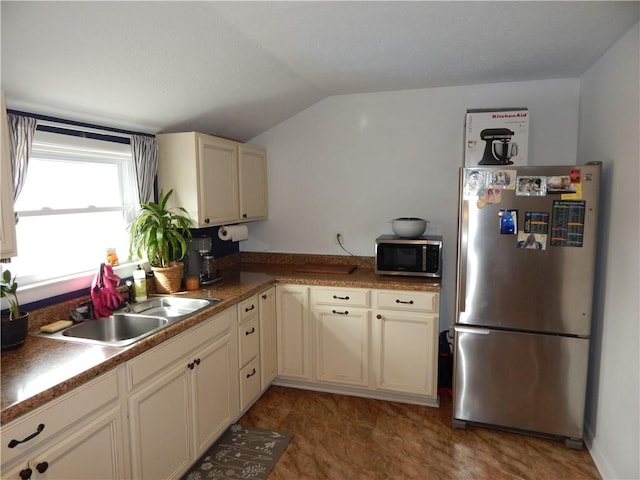 kitchen featuring a sink, stainless steel appliances, lofted ceiling, and cream cabinets