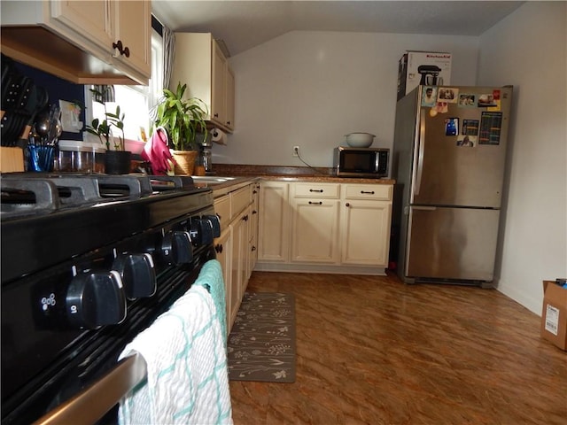 kitchen with vaulted ceiling, cream cabinetry, and appliances with stainless steel finishes