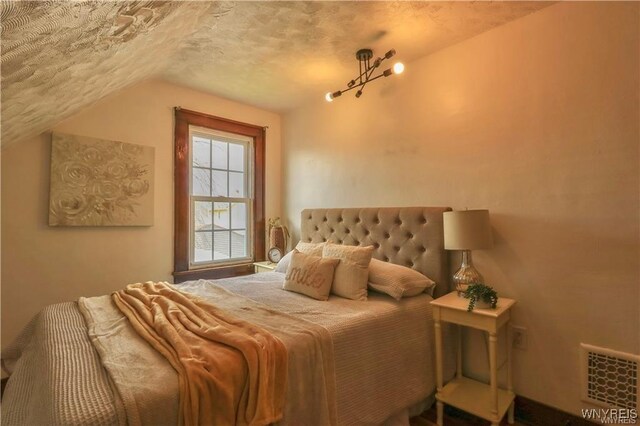 bedroom featuring lofted ceiling, visible vents, and a textured ceiling