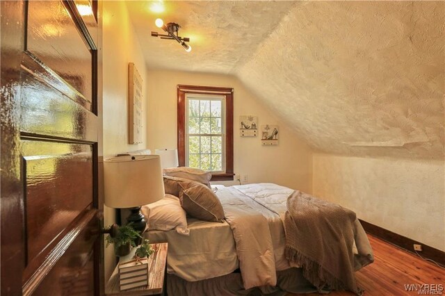 bedroom featuring a textured ceiling, baseboards, wood finished floors, and lofted ceiling