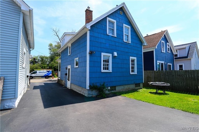 view of side of property featuring a chimney, fence, and a yard