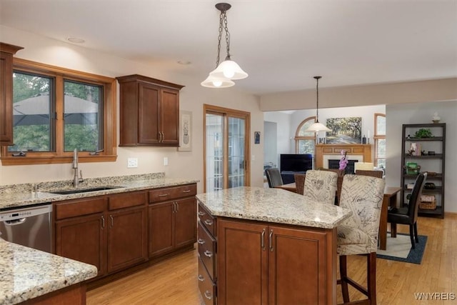 kitchen featuring stainless steel dishwasher, light wood-style flooring, a sink, and decorative light fixtures