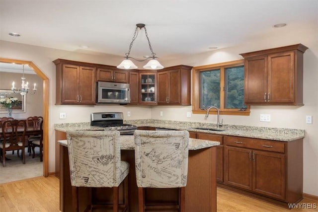 kitchen featuring glass insert cabinets, light stone counters, stainless steel appliances, and a sink