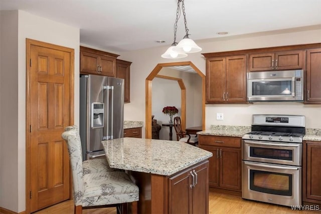 kitchen with stainless steel appliances, decorative light fixtures, a breakfast bar area, and light stone countertops