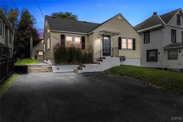 bungalow with driveway, a shingled roof, and a front yard