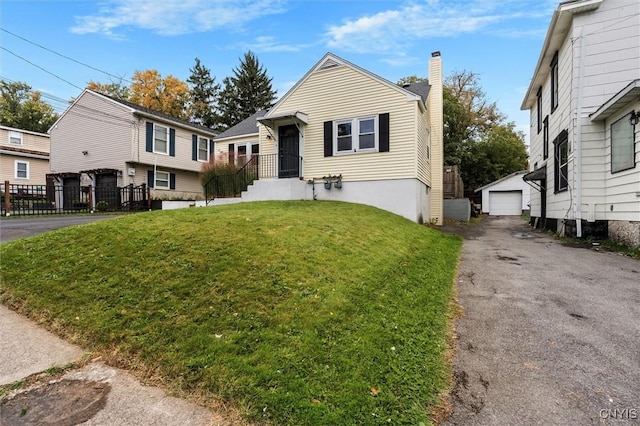 view of front of house featuring a detached garage, a chimney, a front yard, driveway, and an outdoor structure