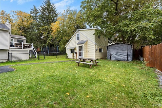 view of yard with a trampoline, an outbuilding, fence, and a wooden deck