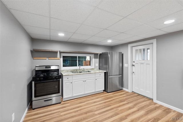 kitchen with light wood finished floors, appliances with stainless steel finishes, white cabinets, a sink, and baseboards