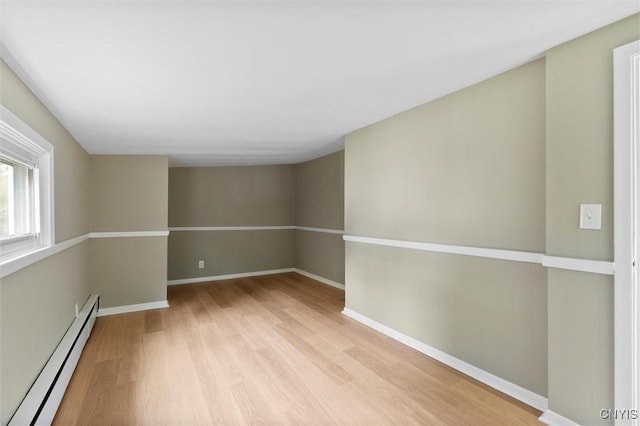 empty room with light wood-style floors, a baseboard radiator, and baseboards