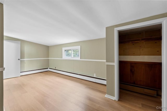 empty room featuring a baseboard radiator, wood finished floors, and wainscoting