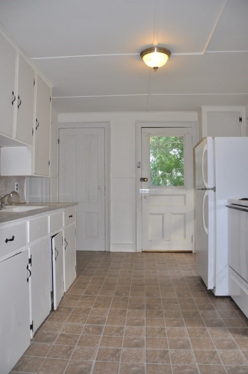 kitchen featuring light countertops, white cabinets, a sink, and freestanding refrigerator