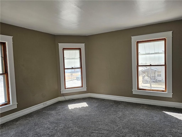 spare room with baseboards and dark carpet