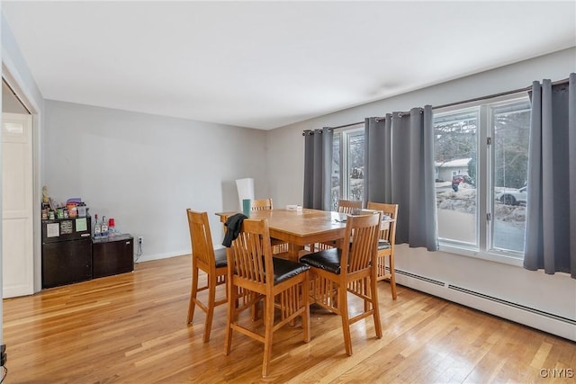 dining room featuring a baseboard heating unit, light wood-type flooring, a wealth of natural light, and baseboards