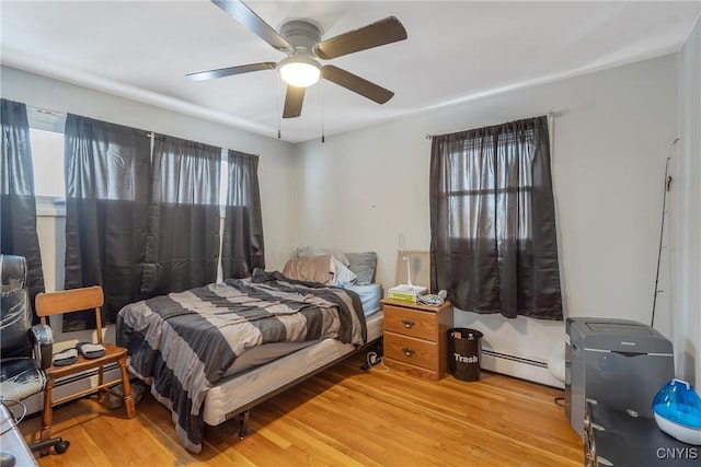 bedroom featuring light wood-style floors, a baseboard heating unit, and a ceiling fan