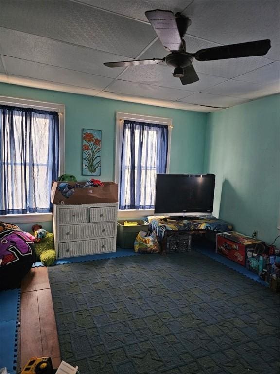 rec room with a healthy amount of sunlight, ceiling fan, dark carpet, and a paneled ceiling