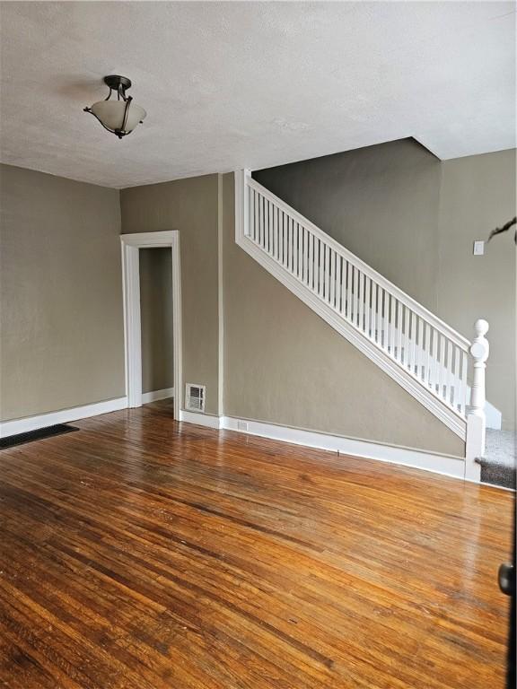 unfurnished living room featuring a textured ceiling, wood finished floors, visible vents, baseboards, and stairs