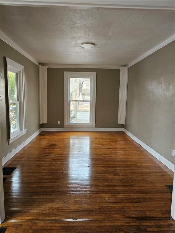 empty room with baseboards, a textured ceiling, ornamental molding, and wood finished floors