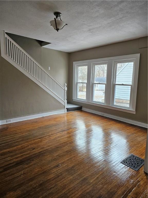 unfurnished living room featuring a textured ceiling, stairway, hardwood / wood-style flooring, and baseboards