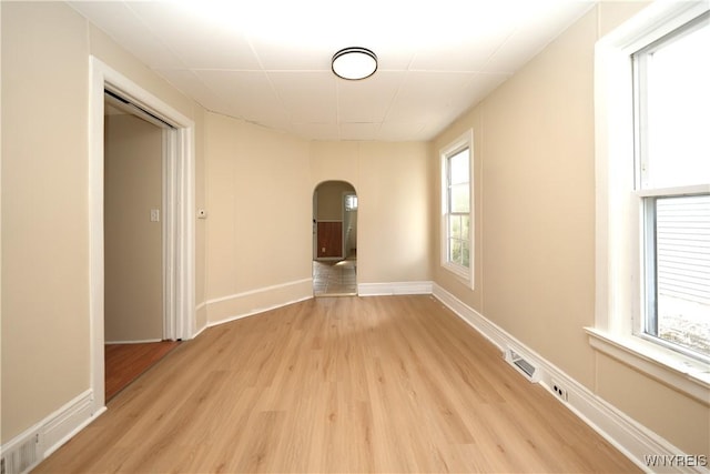 spare room with light wood-type flooring, arched walkways, visible vents, and baseboards