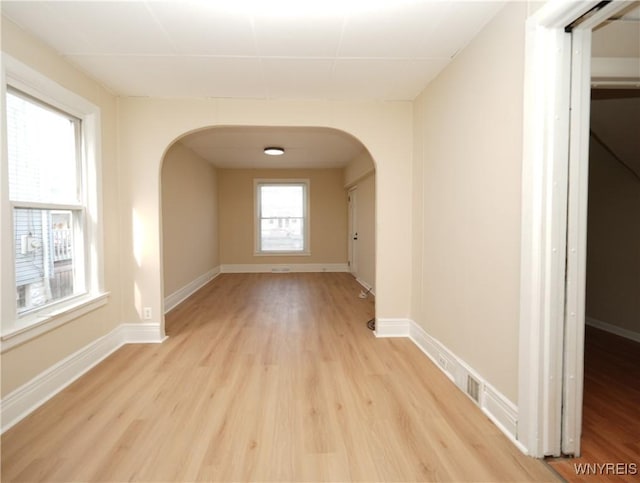 interior space with light wood finished floors, baseboards, and arched walkways