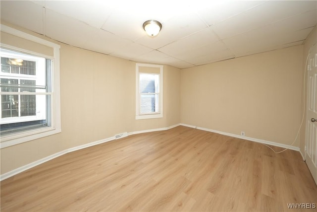 spare room with light wood-type flooring, visible vents, baseboards, and a paneled ceiling