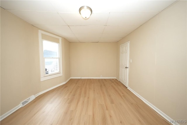 spare room with a paneled ceiling, light wood-style floors, baseboards, and visible vents