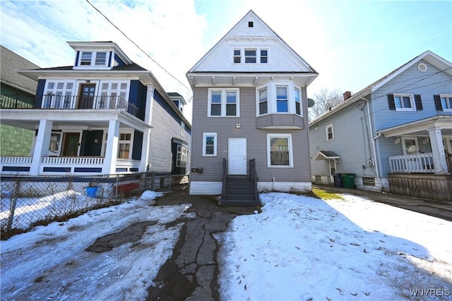 snow covered back of property with a balcony, fence, and entry steps