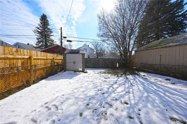 snowy yard featuring a fenced backyard, a storage unit, and an outbuilding