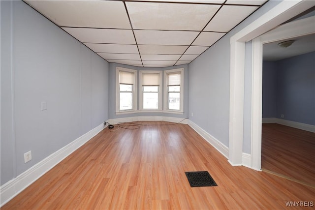 empty room featuring light wood-style floors, a paneled ceiling, visible vents, and baseboards