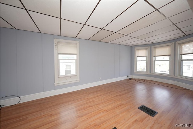 empty room with a wealth of natural light, a paneled ceiling, wood finished floors, and visible vents