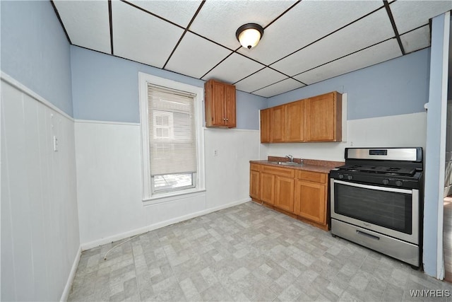 kitchen featuring a paneled ceiling, a sink, light floors, brown cabinetry, and gas stove