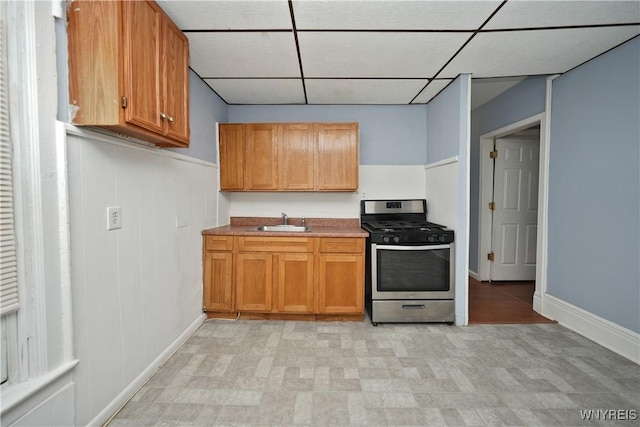 kitchen featuring a paneled ceiling, stainless steel range with gas cooktop, brown cabinets, and a sink