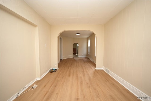 corridor with arched walkways, light wood-style flooring, and baseboards