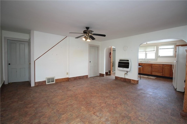 unfurnished living room with arched walkways, heating unit, visible vents, a ceiling fan, and baseboards