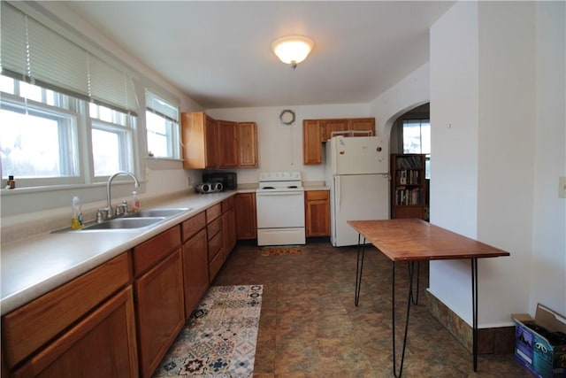 kitchen featuring white appliances, arched walkways, brown cabinets, light countertops, and a sink