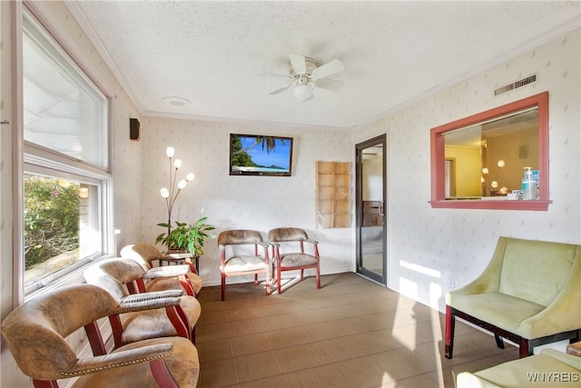 living area featuring a textured ceiling, ornamental molding, visible vents, and wallpapered walls