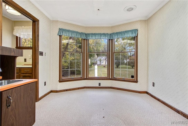 unfurnished dining area featuring ornamental molding, a wealth of natural light, carpet flooring, and a sink