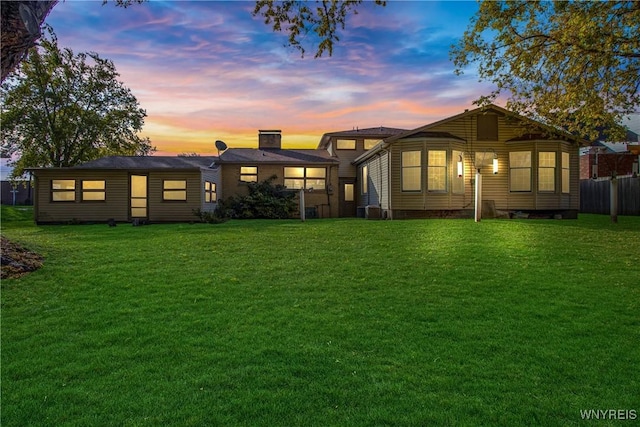 back of property at dusk featuring a chimney, fence, and a yard