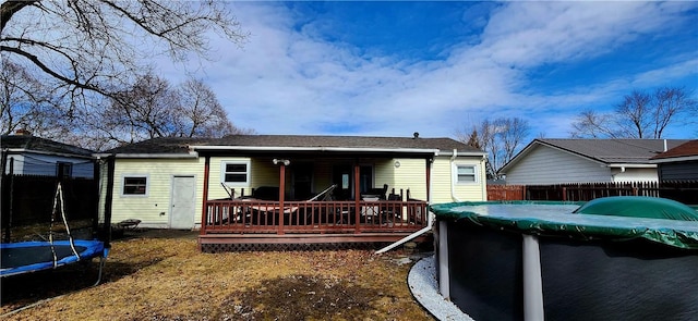 rear view of property featuring a trampoline, fence, a deck, and a fenced in pool