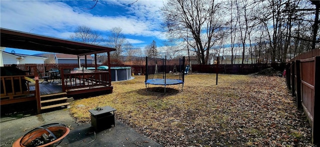 view of yard with a deck, a trampoline, and a fenced backyard