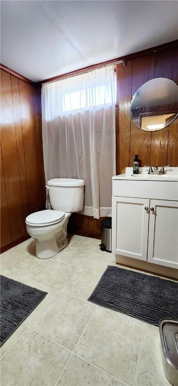 bathroom featuring wood walls, tile patterned flooring, vanity, and toilet