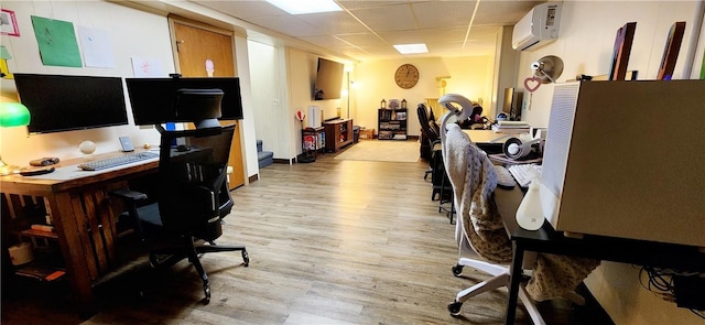 office space featuring a wall unit AC, light wood-type flooring, and a drop ceiling