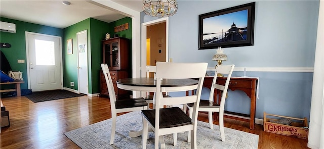 dining space with a chandelier, a wall mounted AC, wood finished floors, and baseboards