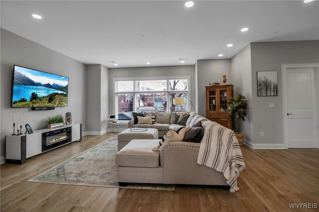 living room featuring recessed lighting, a glass covered fireplace, baseboards, and wood finished floors