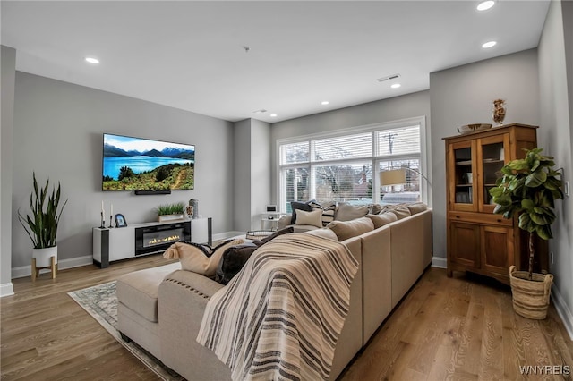 living room featuring light wood-style flooring, recessed lighting, visible vents, baseboards, and a glass covered fireplace