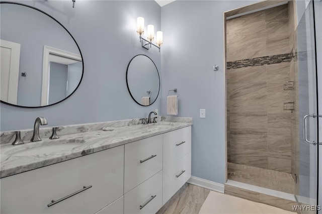 full bathroom with baseboards, double vanity, a sink, and a shower stall